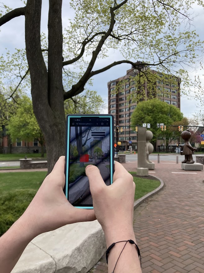 View over the shoulder of a person holding up a phone in front of a large sculpture of two figures